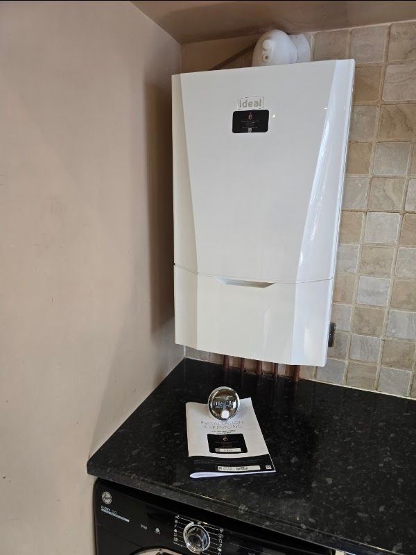 New white Ideal combi boiler installed above a black granite worktop with its commissioning document and magnetic filter in place — example image